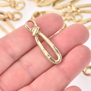 May include: Gold-toned metal toggle clasp with a knotted design. The clasp is smooth and has a hammered texture.