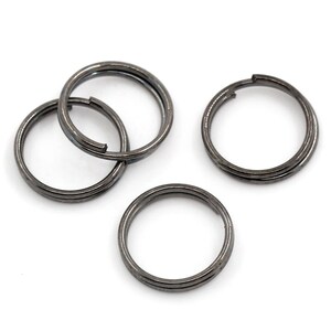 May include: Several gunmetal-colored split key rings are arranged against a white background. Each ring is circular with a split for attaching keys or other items. The rings have a simple, functional design.