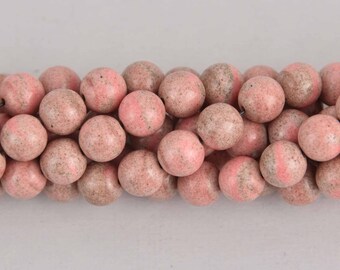 May include: Strand of round, pink beads with speckled, earthy tones. The beads have a smooth, polished appearance and are strung together, suggesting they are for jewelry making or crafting. The color palette is soft and natural.