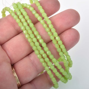 May include: A strand of light green faceted glass beads. The beads are small and round, and they have a slight shimmer to them.