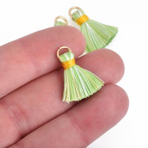 May include: Three green and white striped tassels with gold jump rings. The tassels have a yellow band at the top.