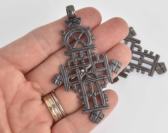 May include: A silver-toned Ethiopian Orthodox cross pendant with intricate geometric designs. The cross is made of metal and has a loop at the top for hanging.