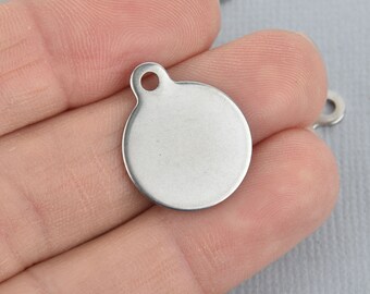 May include: A silver round metal charm with a hole at the top. The charm is blank and can be used for jewelry making or other crafts.