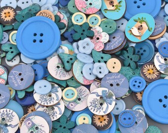 May include: A collection of assorted buttons in various shades of blue, teal, and white. The buttons feature diverse shapes including circles, flowers, and hearts, with some displaying printed illustrations of lavender, birds, and birdhouses.