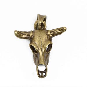 May include: A gold-toned metal bull skull pendant with detailed horns and a hollowed-out skull design.