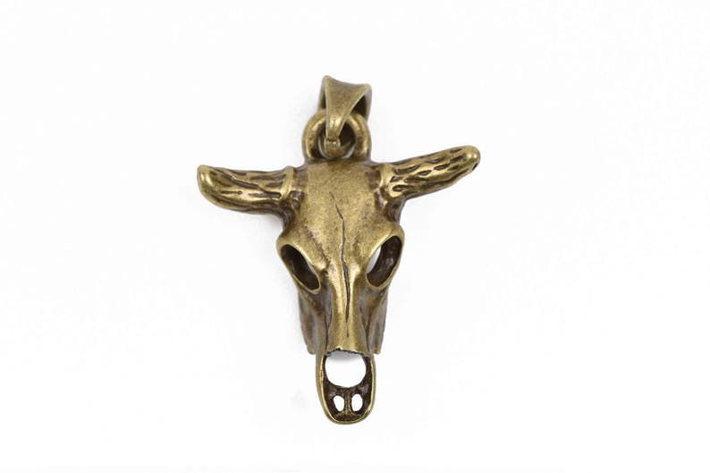 May include: A gold-toned metal bull skull pendant with detailed horns and a hollowed-out skull design.