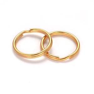 May include: Two gold-colored split key rings, interlocked, against a white background. Each ring has a split opening for attaching keys or other items. The rings are made of a shiny, metallic material.