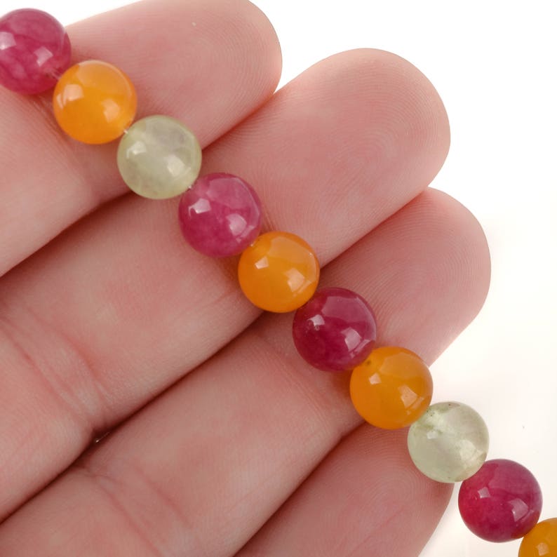 Puede incluir: Primer plano de una pulsera de cuentas con una hebra de cuentas redondas y coloridas. Las cuentas son en tonos de rojo, naranja y verde claro. La pulsera est&aacute; sujeta en la mano de una persona.