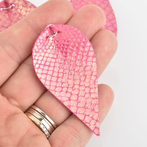 May include: A pair of pink leather earrings with a snakeskin pattern. The earrings are teardrop shaped and have a silver hook.