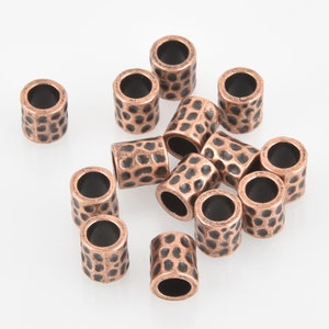 May include: A group of 14 copper-colored metal beads with a hammered texture. The beads are round with a hole in the center. They are scattered on a white surface.