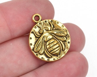 May include: Gold-toned metal charm featuring a detailed bee design. The bee is centered on a round charm with a textured border.