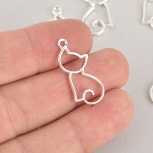 May include: Silver-toned metal charm in the shape of a cat. The charm is hollow and has a smooth, shiny finish.
