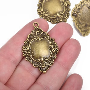 May include: A set of three antique gold-toned metal charms with ornate floral designs. Each charm features a blank oval space in the center, perfect for adding a personalized touch.