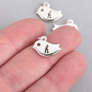 May include: Silver bird-shaped charm pendants, each with a small loop for attaching to a chain or bracelet. The charms have a smooth, reflective surface and feature the lowercase letter "h" in black script.