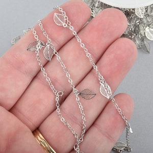 May include: Silver chain with delicate leaf charms. The chain is made of metal and has a polished finish. The leaves are evenly spaced along the chain.