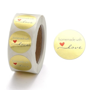 Puede incluir: Rollo de pegatinas de lámina dorada con el texto "hecho a mano con amor" y un corazón rojo.