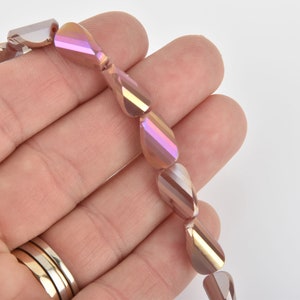 May include: A strand of iridescent teardrop-shaped beads. The beads have a pearlescent finish with hues of pink, gold, and brown. Each bead is faceted, catching light to create a shimmering effect. The beads are strung together, ready for jewelry making.
