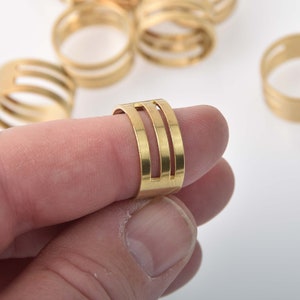 May include: Gold metal ring with three horizontal cutouts. The ring is worn on a finger.