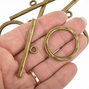 May include: Antique brass toggle clasps with a round ring and a straight bar. The clasps have a smooth, aged finish and are perfect for jewelry making or other craft projects.