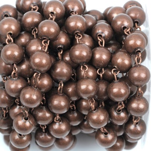 May include: A roll of copper-colored chain with round beads. The chain is made of metal and the beads are smooth and shiny.