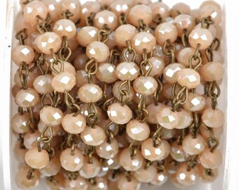 May include: A close-up of a chain of light peach-colored faceted glass beads strung on a brass chain. The chain is coiled and ready to be used for jewelry making.