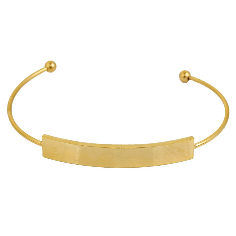 May include: A gold-colored cuff bracelet with a rectangular center plate. The bracelet has a simple, elegant design with rounded ends and a smooth, polished finish. The overall style is minimalist and modern.