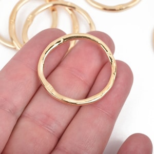 May include: Close-up of several gold-colored, irregular-shaped rings. The rings have a textured surface and a slightly uneven shape. The rings are on a white background. The rings appear to be jewelry components or craft supplies.