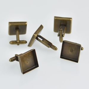 May include: Five antique brass-toned square cufflinks. The cufflinks have a classic design with a rectangular base and a T-bar closure. The metal has a slightly aged appearance.