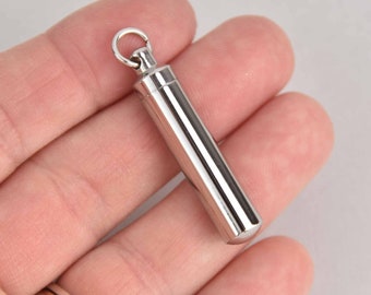 May include: A silver metal pendant with a cylindrical shape and a small loop at the top. The pendant is about 2 inches long.