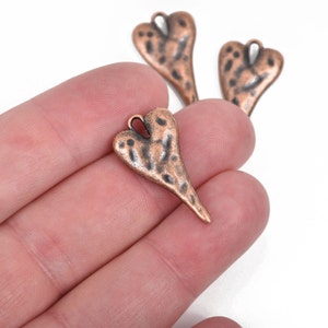 May include: Three antique copper-toned heart-shaped charms with a hammered texture. The charms have a loop at the top for attaching to jewelry or other crafts.