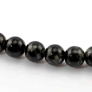 May include: A strand of polished, round black beads with subtle gray and green inclusions. The beads have a glossy finish and are evenly sized, suggesting they are part of a necklace or bracelet.