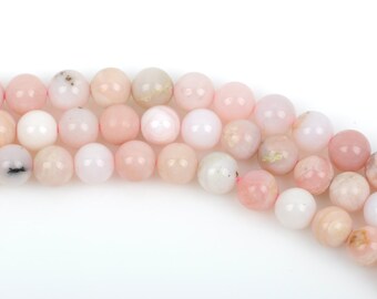 May include: Strands of pink opal gemstone beads. The beads vary in shades of pink, from pale to deeper hues, with some showing subtle patterns. The round beads are strung together, creating a natural and elegant look.