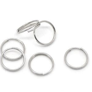 May include: A collection of silver-colored split key rings. The key rings are round and have a split opening for attaching keys or other items. The key rings are made of metal and are arranged on a white background.