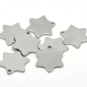 May include: A collection of seven silver-colored, six-pointed star charms. Each charm has a small hole at the top for stringing. The charms are displayed against a white background.
