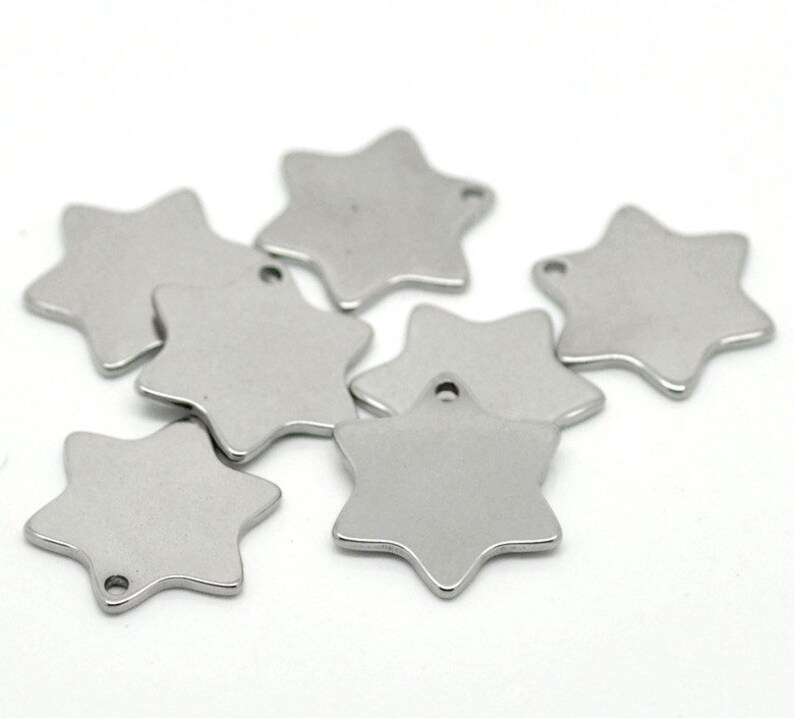 May include: A collection of seven silver-colored, six-pointed star charms. Each charm has a small hole at the top for stringing. The charms are displayed against a white background.