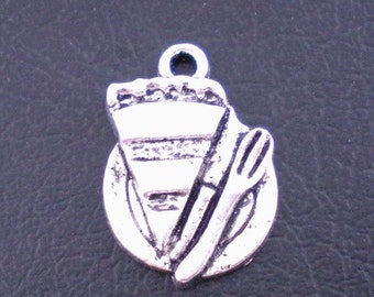 May include: Silver-toned charm featuring a slice of pie on a plate, with a fork and knife. The charm has a loop at the top for attaching to a necklace or bracelet. The pie slice has a textured crust.