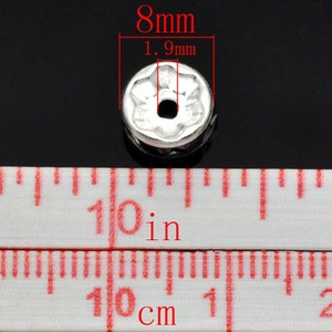 Puede incluir: Cuente de metal plateado con dise&ntilde;o de flor, que mide 8 mm de di&aacute;metro y 1,9 mm de alto. La cuenta tiene un agujero en el centro para enhebrar.