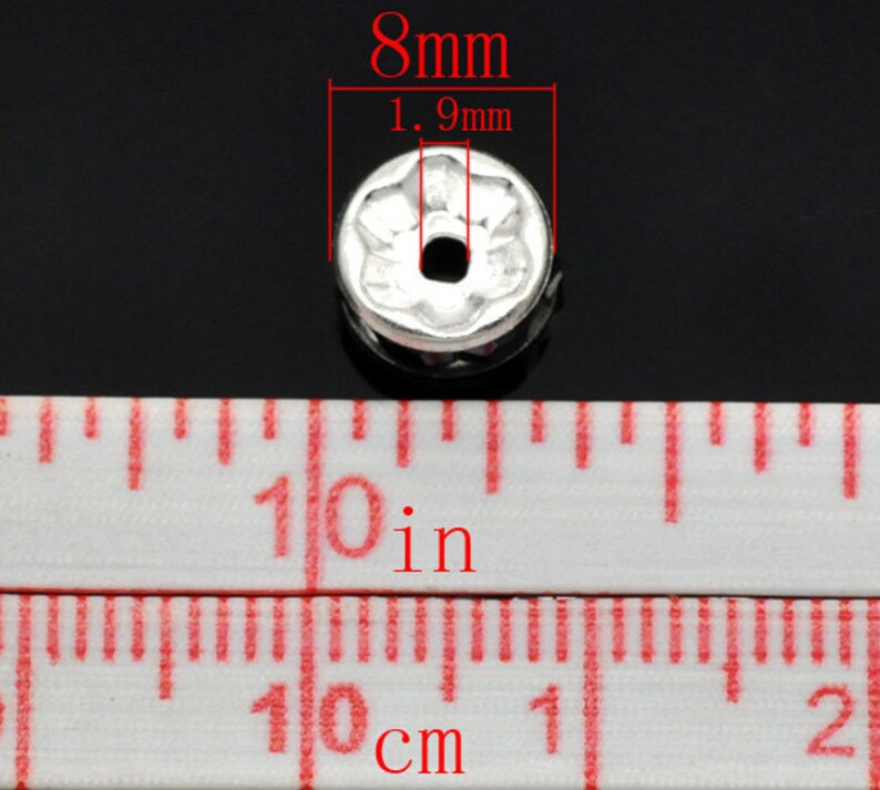 Puede incluir: Cuente de metal plateado con dise&ntilde;o de flor, que mide 8 mm de di&aacute;metro y 1,9 mm de alto. La cuenta tiene un agujero en el centro para enhebrar.