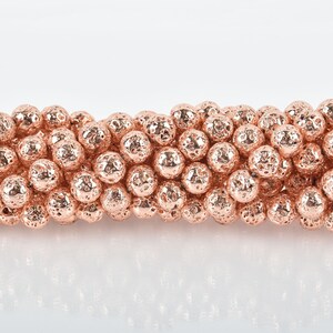 May include: Close-up of a strand of rose gold lava rock beads. The beads have a textured, porous surface and a metallic sheen. These round beads are ideal for jewelry making, such as bracelets and necklaces.