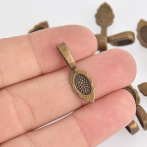May include: Bronze-colored metal pendant findings with an oval, textured design. The findings have a loop at the top for attaching to a chain or other jewelry component. The findings are small, measuring approximately 0.75 inches in length.