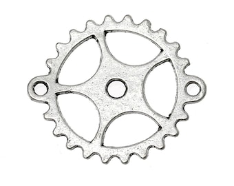 May include: A silver-colored metal gear with a steampunk aesthetic. The gear has a circular shape with multiple spokes and a central hole. Two small loops extend from the sides. The gear's surface has a slightly aged, textured appearance.