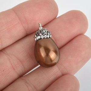 May include: A brown teardrop-shaped pearl pendant with a silver setting and clear rhinestones.