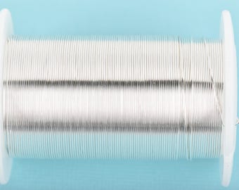 May include: A spool of silver-colored wire on a white plastic bobbin. The wire is wound tightly around the bobbin, creating a smooth, continuous surface.