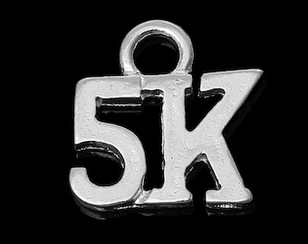 May include: A silver-colored charm in the shape of the text "5K" with a loop at the top for attaching to a necklace or bracelet. The charm is designed with a simple, bold font and is set against a black background.