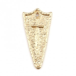 May include: Gold-toned metal charm shaped like a shield with a sword inside. The shield has a textured surface and a hole at the top for hanging.