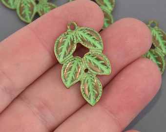Può includere: Un ciondolo a forma di foglia verde e marrone con un anello per appenderlo. Il ciondolo ha una finitura in smalto verde chiaro con accenti marroni sulle foglie. Il ciondolo è probabilmente per la creazione di gioielli o altri lavori artigianali.