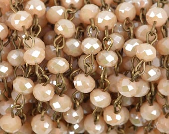 May include: A close-up of a strand of beige faceted glass beads strung on a brass chain. The beads are small and round, and the chain is delicate.