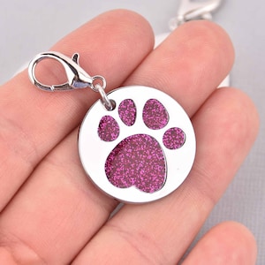 May include: Silver dog tag with a pink glitter paw print design. The tag has a silver swivel clasp.