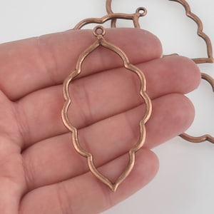 May include: A copper-colored metal pendant with a scalloped edge and a loop at the top for hanging. The pendant is shaped like a teardrop and has a delicate, intricate design.