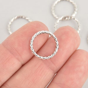 May include: Silver-toned metal jump rings with a twisted rope design. The rings are approximately 1 inch in diameter.